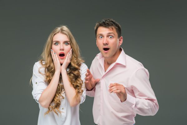 Portrait of a young surprised couple standing against gray studio background